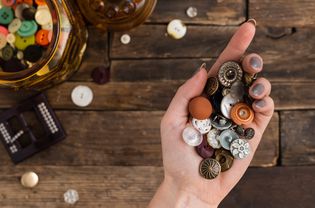 Variety of old-fashioned buttons in palm of hand over wood surface