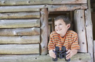 男孩在木制游戏室拿着双筒望远镜