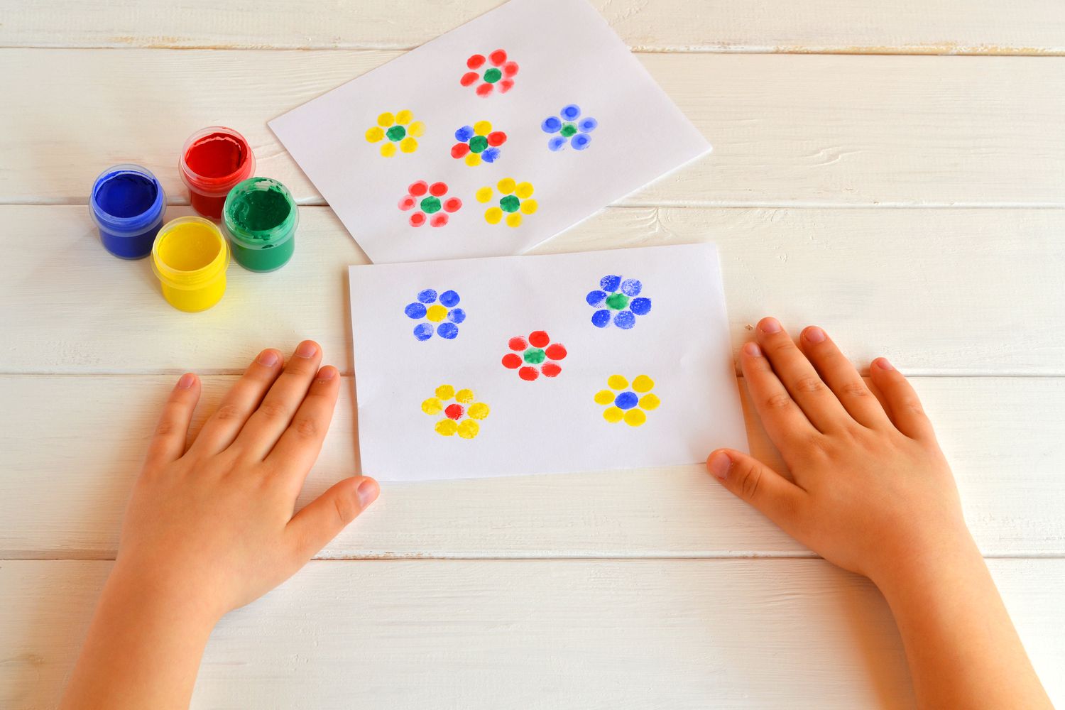 两幅画着孩子手指上的花。水粉罐子。孩子们的手放在桌子上。夏天孩子手指画的想法