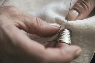 person sewing with needle and thimble