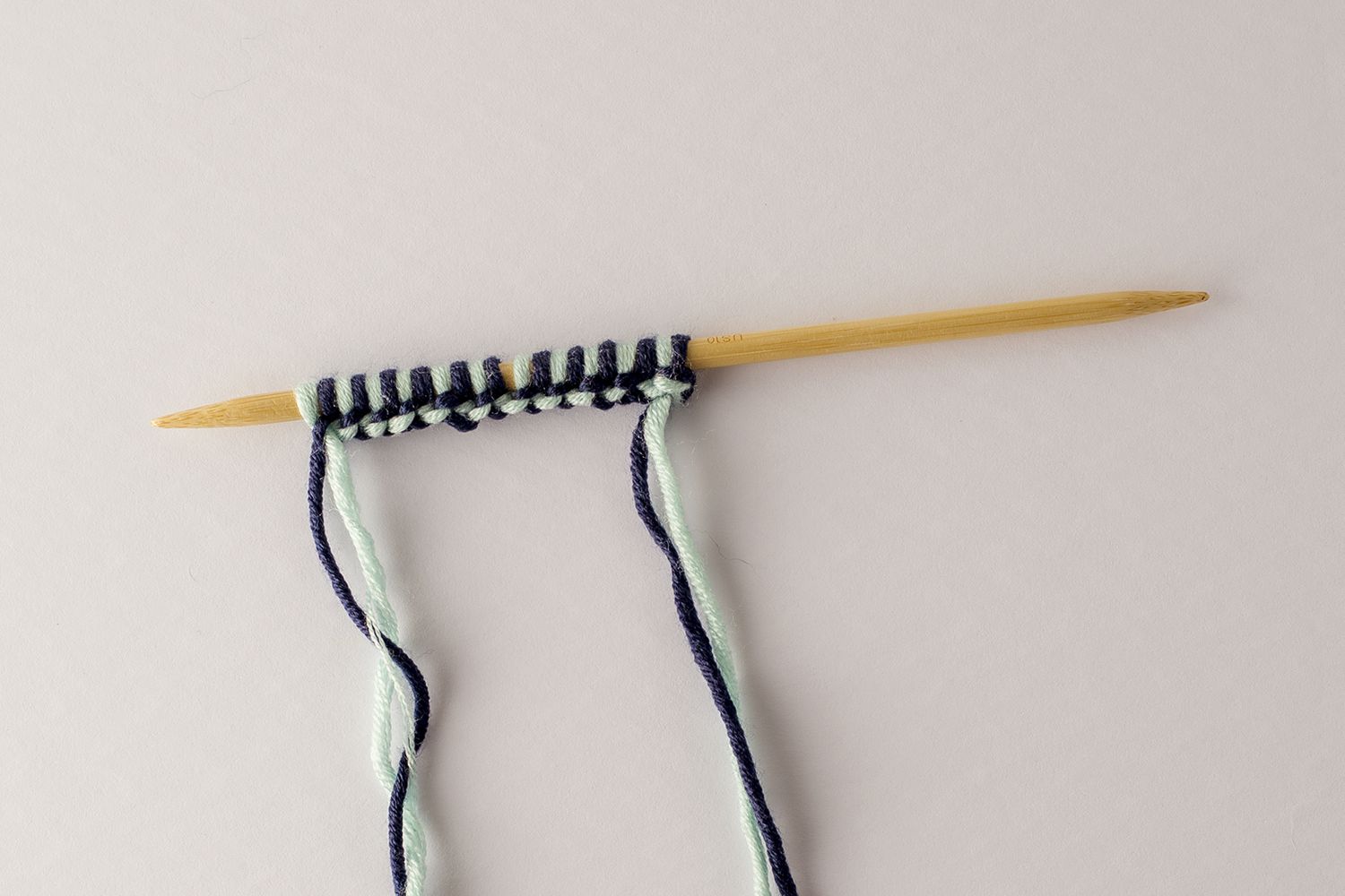 两种颜色的纱线在木制针织针上绕成一圈。