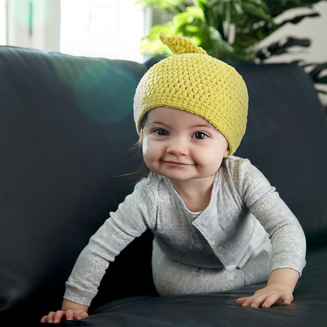 黄色钩针婴儿帽子小女孩爬在沙发上。