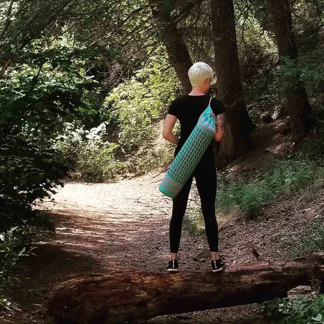 一个女人在树林里穿着编织的瑜伽垫包