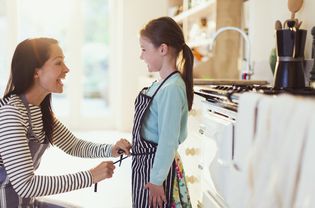 A mom tying her daughter's apron strings in a kitchen