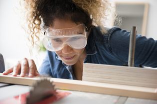 Woman wearing safety goggles while cutting wood