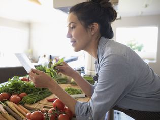 微笑的拉丁裔女性与蔬菜阅读食谱在厨房