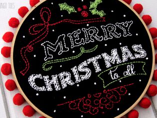 圣诞快乐粉笔艺术刺绣图案在黑色织物和放置在刺绣箍。