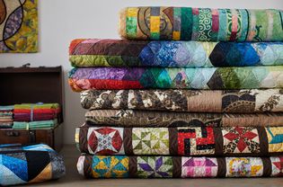 Quilts stacked and wooden chest with stacks of fat quarters on white wall background