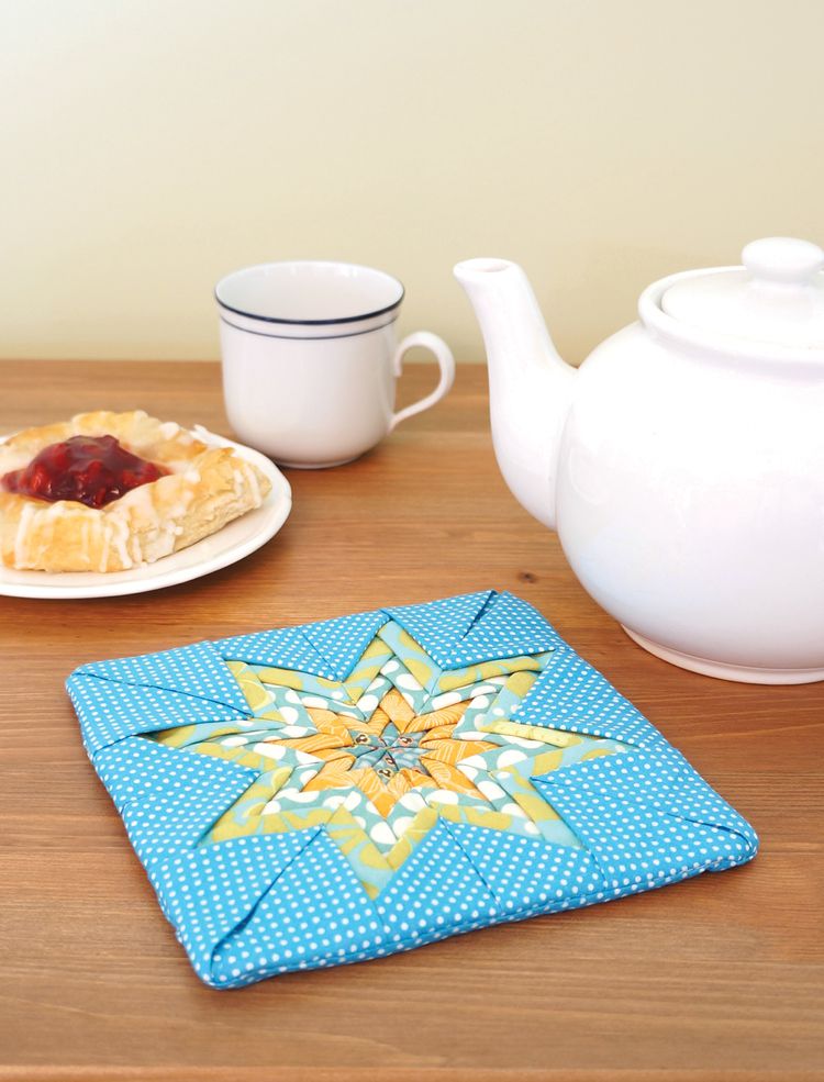 一个黄蓝相间的折叠星形壶架，旁边放着一个茶壶和丹麦饼