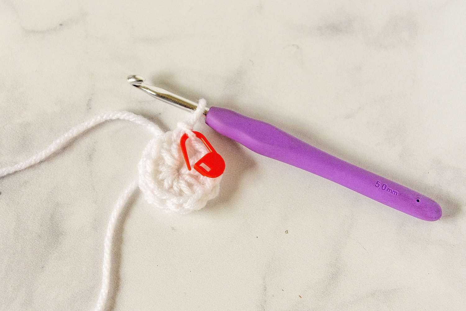Crochet circle with red stitch marker and crochet hook.
