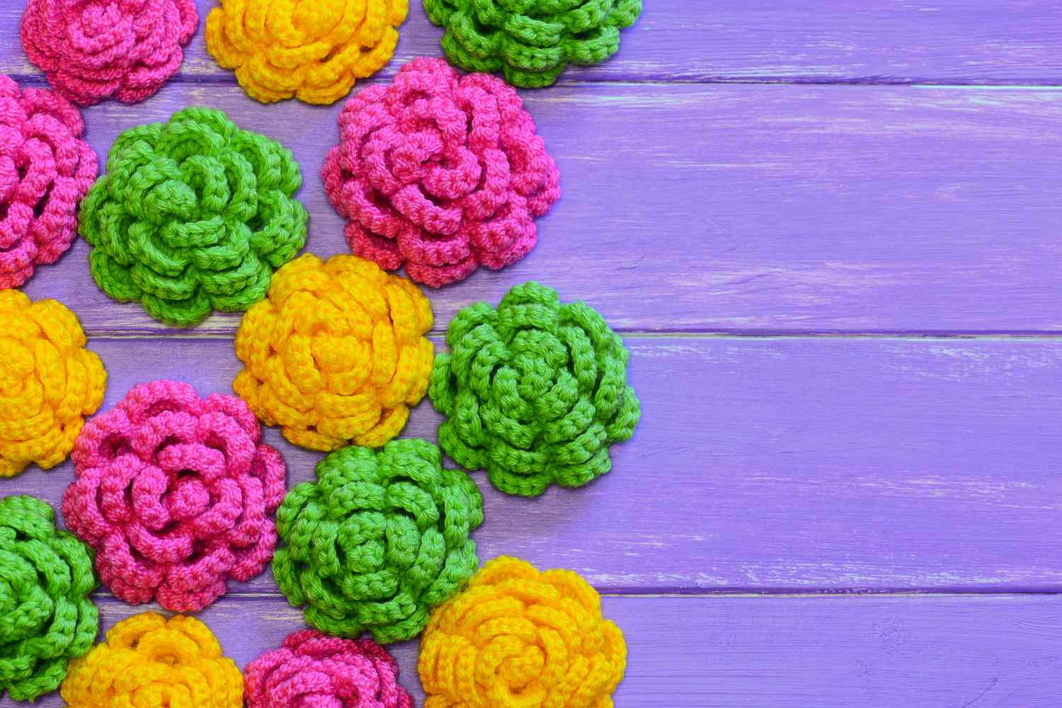 Crocheted flowers. Yellow, pink and green crocheted flowers. Multicolored floral ornaments. Bright background. Closeup