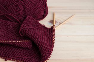 Woolen burgundy yarn knitting on wooden table