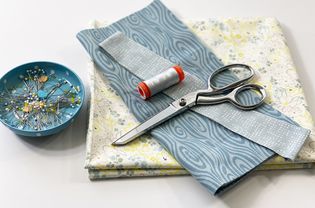Fabric, scissors, thread, and pins on a table