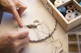 生活方式理念，在家工作，重塑你的生活:在轻木桌上用石珠和工具制作流苏结珠宝的女性手特写