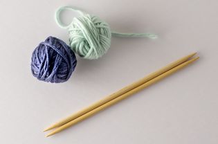 Two balls of yarn and wood knitting needles on a white background.