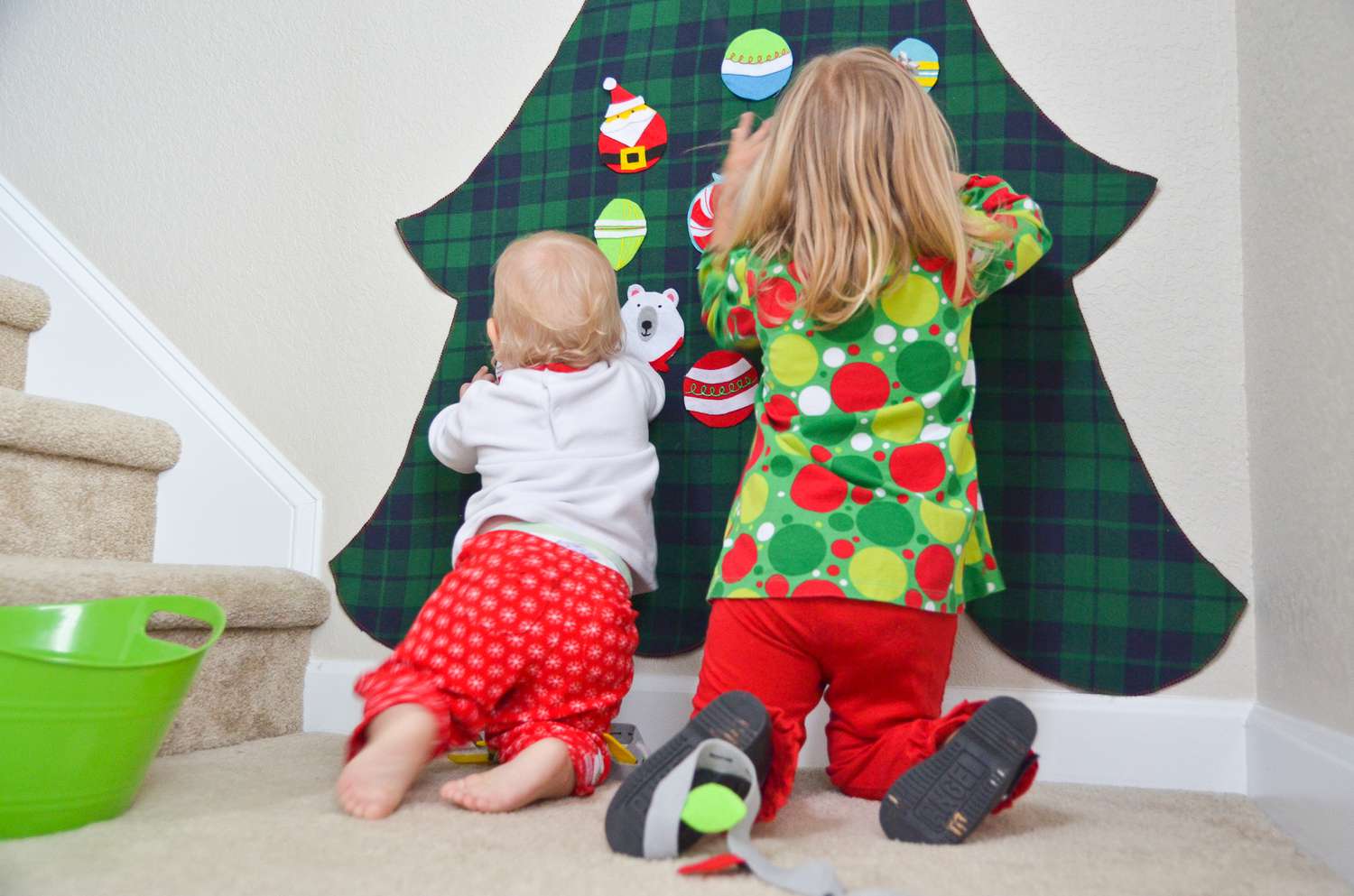两个孩子把毛毡饰品挂在墙上的毛毡圣诞树上。