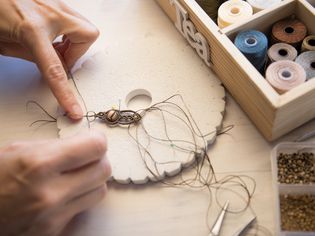 生活方式的概念，在家工作，重塑你的生活:女人的手在轻木桌上用石珠和工具制作编结珠宝的特写