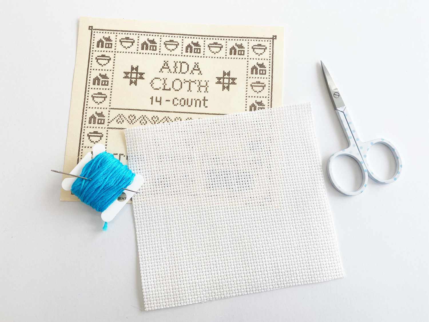 Aida cloth, thread, scissors, and a needle laying on a table
