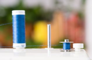 Blue thread spool wrapped around sewing machine bobbin