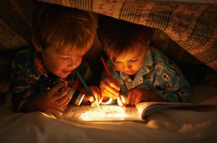 Two boys coloring under the covers at night