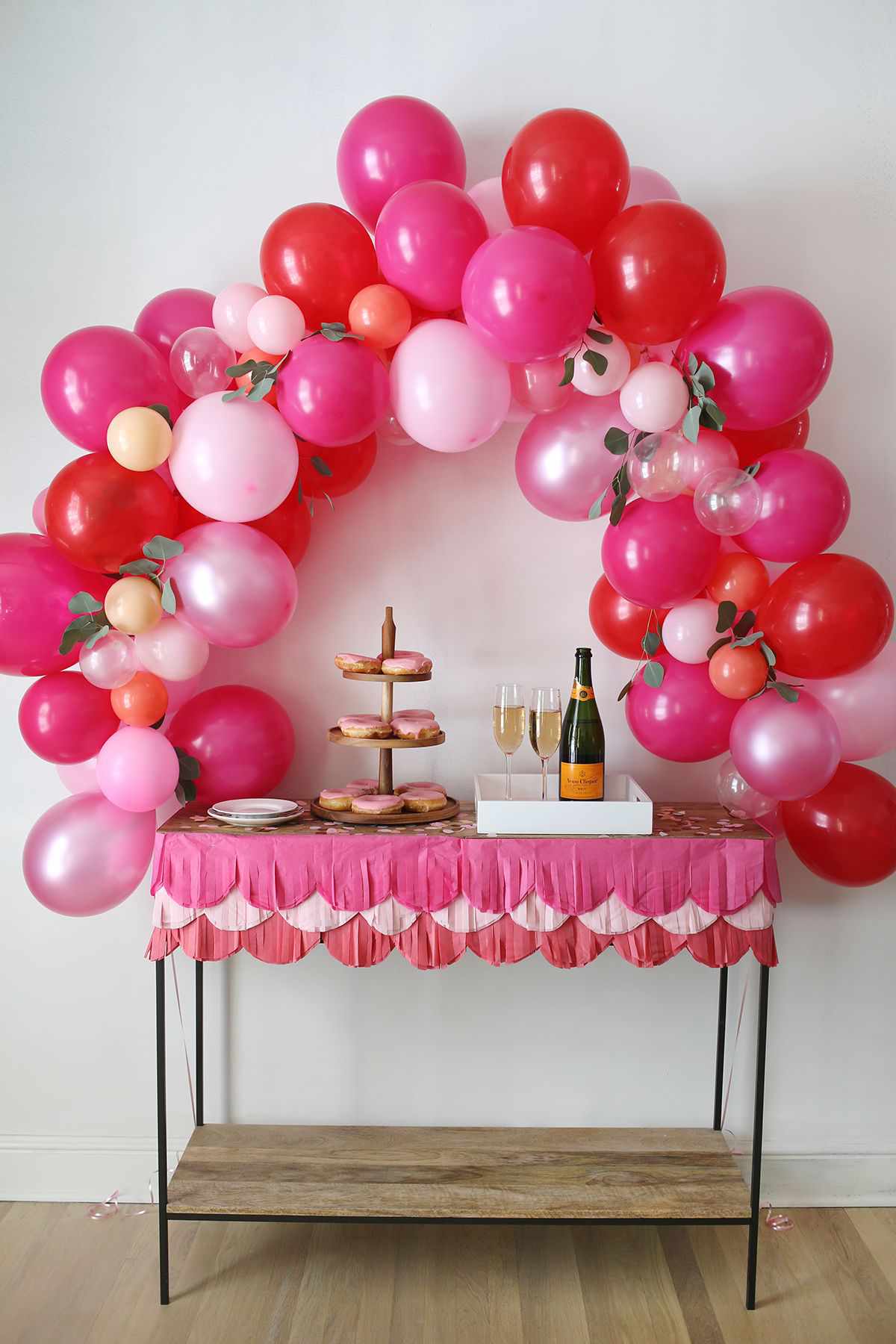 气球拱门上有红色和粉色的气球，上面放着食物和香槟。