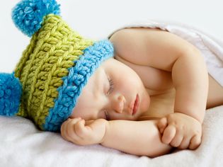 蓝色和绿色钩针编织的婴儿便帽上睡着的婴儿。