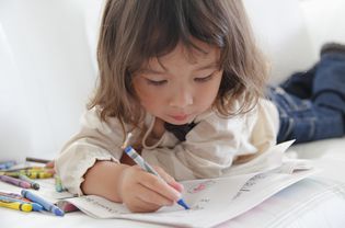 close up of little girl lying on couch coloring