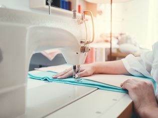 缝纫机和女性的特写视图。年轻裁缝缝和使用布设计工作室。小型企业