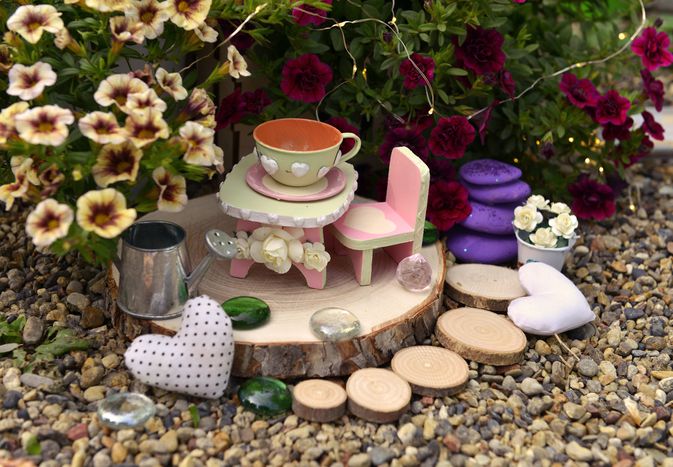 Tiny table, chair and cup by flowerpot with petunia flowers in the garden.