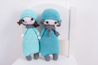 Two handmade crocheted dolls in blue with scarf and hat on a white chair