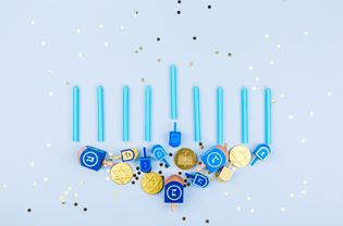 Blue confetti background with menora made of dreidels and chocolate coins. Hanukkah and judaic holiday concept.