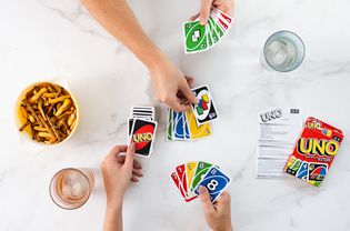 Two people playing the Uno card game next to drinks and snacks