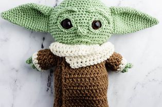 A crocheted baby Yoda laying on a table