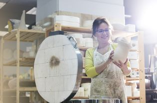 微笑的成熟女子把陶器花瓶在工作室的窑