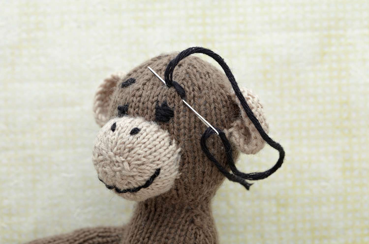 在编织的玩具猴子脸上缝着眉毛