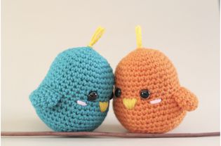 Two small, different colored crochet birds side by side.