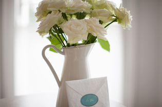 Card leaning against white rose bouquet in pitcher