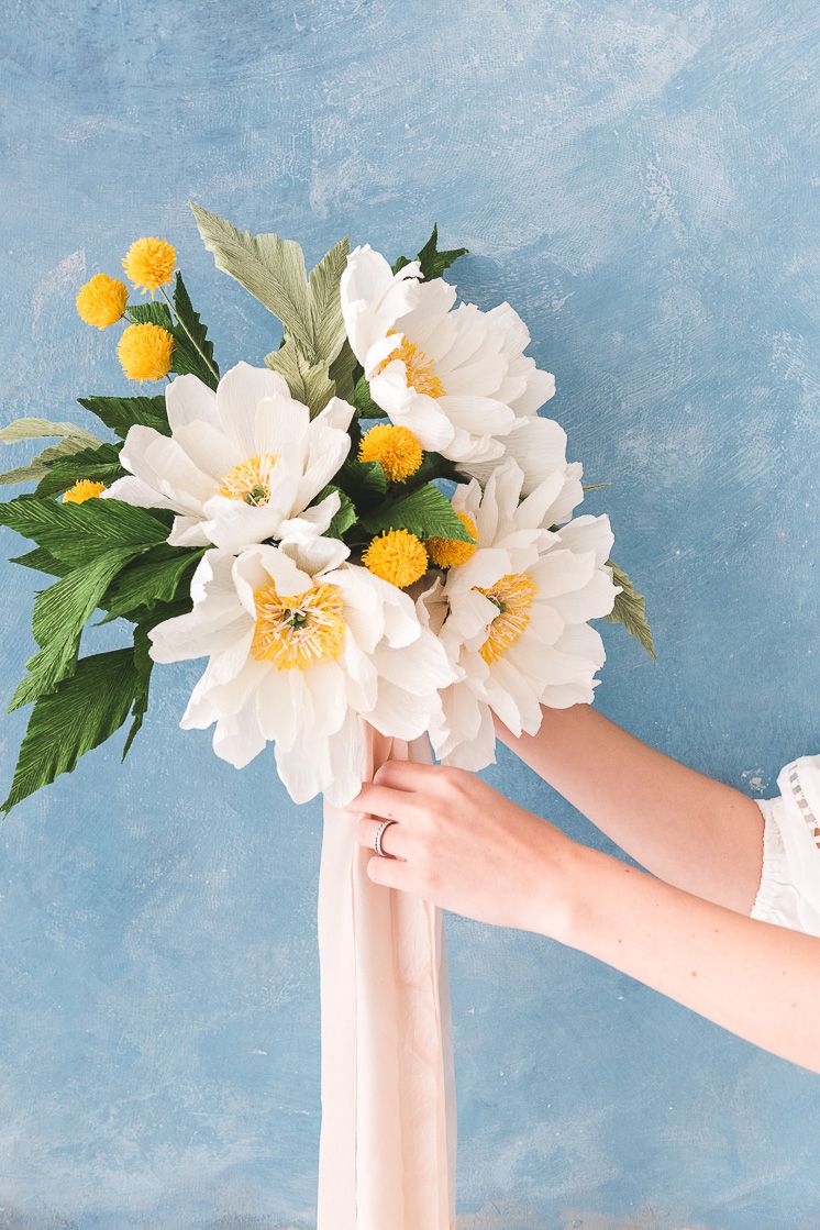 一个女人手里拿着一个白色和黄色纸鲜花花束