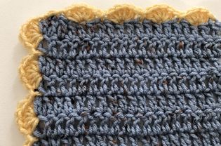 Yellow crochet shell stitch edging around blue yarn.