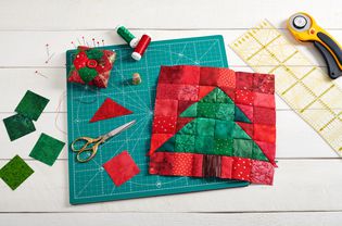 Christmas tree patchwork block, pieces of fabric, quilting and sewing accessories on white wooden background