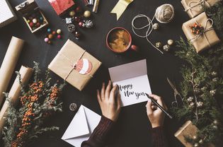 在礼物和装饰品的包围下写新年卡片的人。