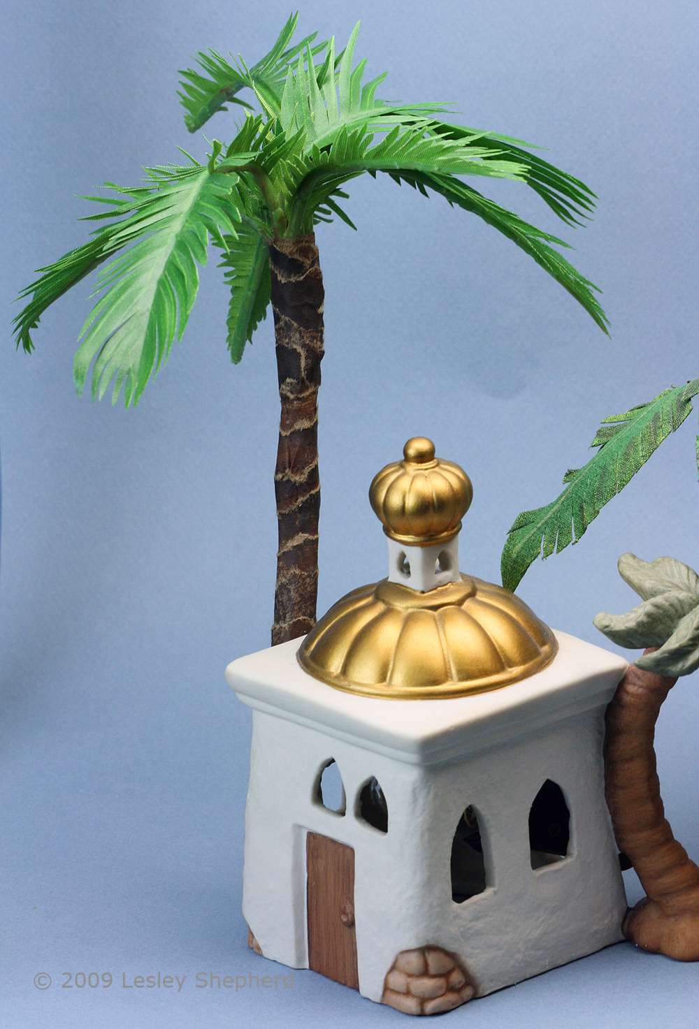 Scale miniature palm tree set behind a porcelain building in a Christmas Nativity set.