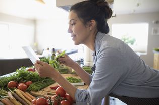 微笑的拉丁妇女与蔬菜阅读食谱在厨房
