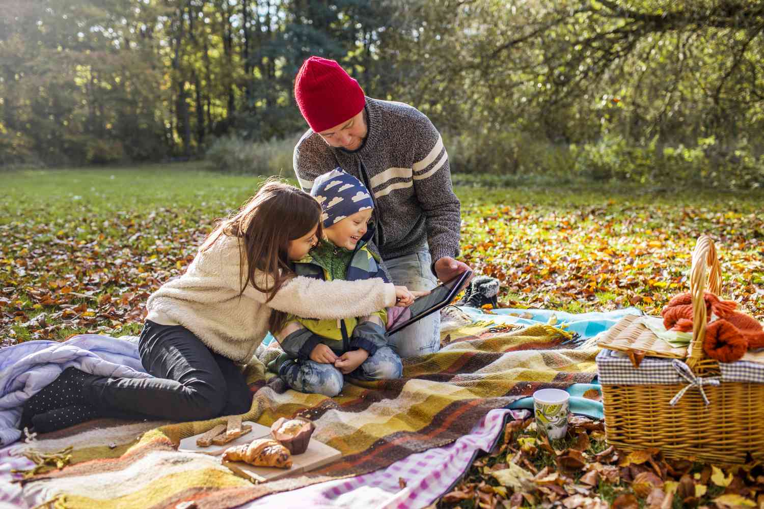 父亲和孩子在森林野餐毯上使用数码平板电脑