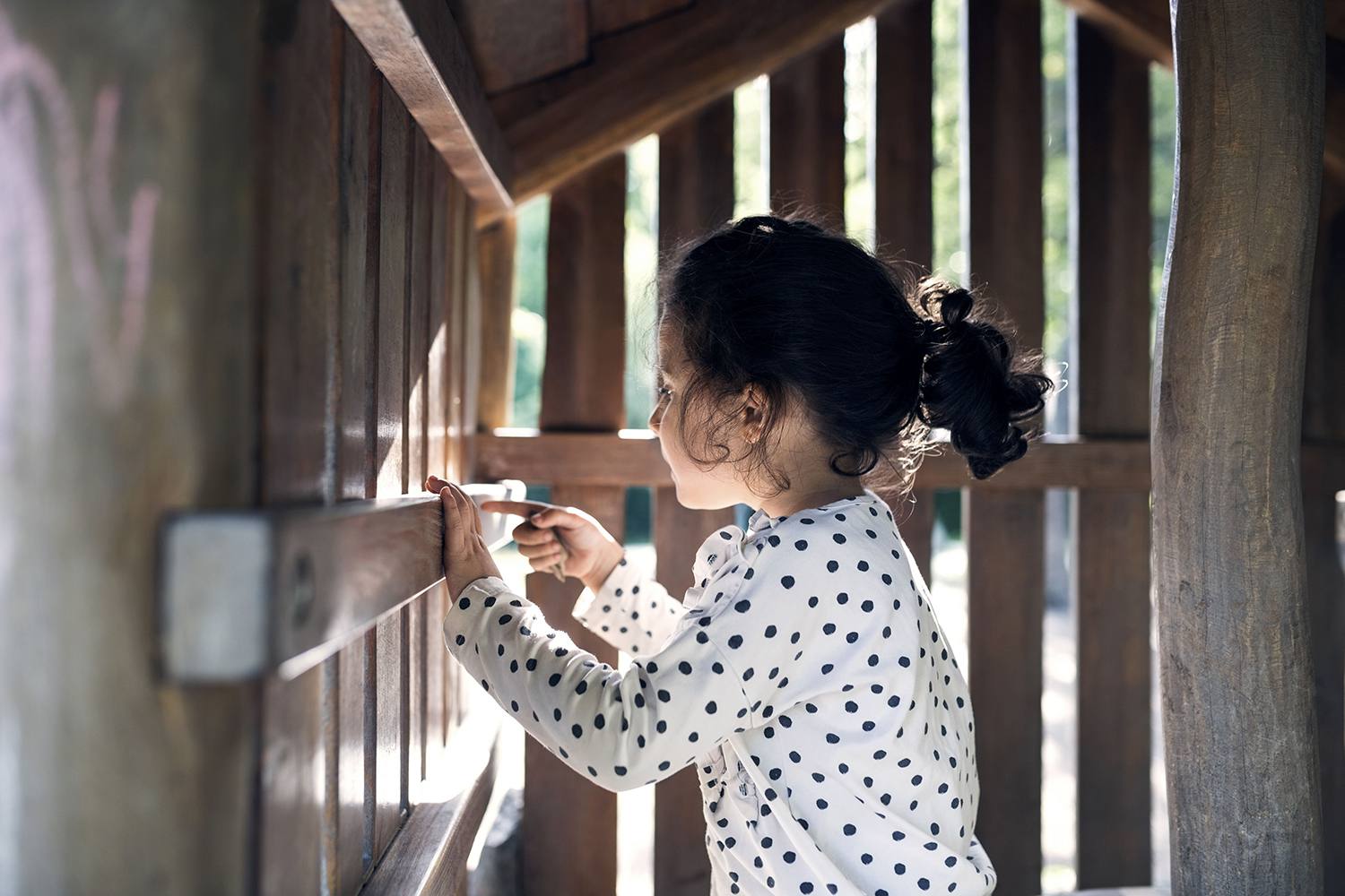 微笑的女孩在木制玩具屋玩耍的侧视图