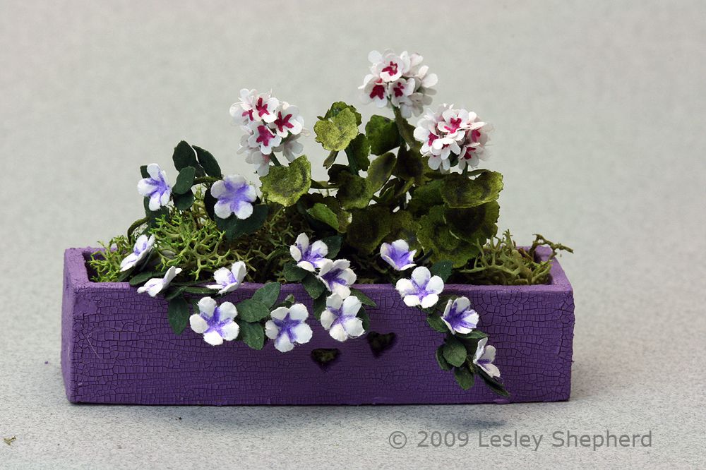 Dolls house plants fill the interior of a painted 1:12 scale window box with heart cutouts.