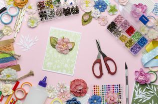 Paper flowers, scissors, homemade card, paper and scrapbooking items on pink background