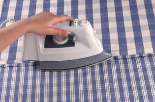 Person using an iron to pressing a seam open on a blue-and-white striped fabric.