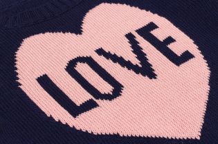 手工编织的蓝色面料与粉红色的心和字爱捆绑在编织针作为背景或纹理