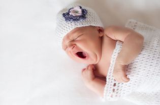 Newborn baby girl yawning in a crocheted outfit